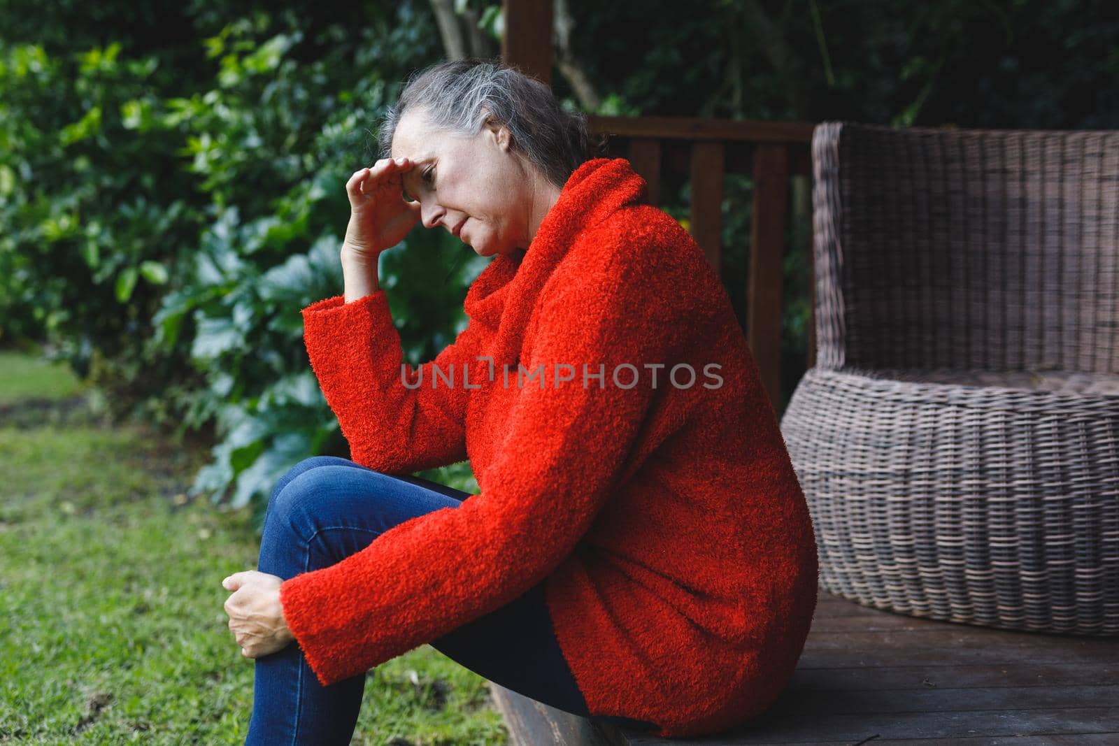 Thoughtful senior caucasian woman sitting with hand on brow looking down in garden. retirement lifestyle, spending time alone at home.