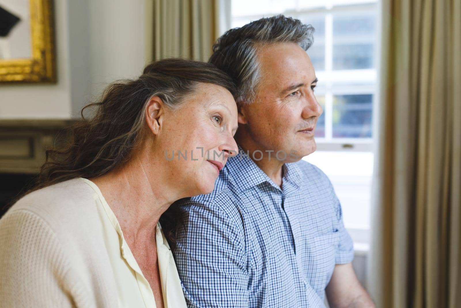 Happy senior caucasian couple sitting on sofa, embracing and smiling. retirement lifestyle, spending time at home.