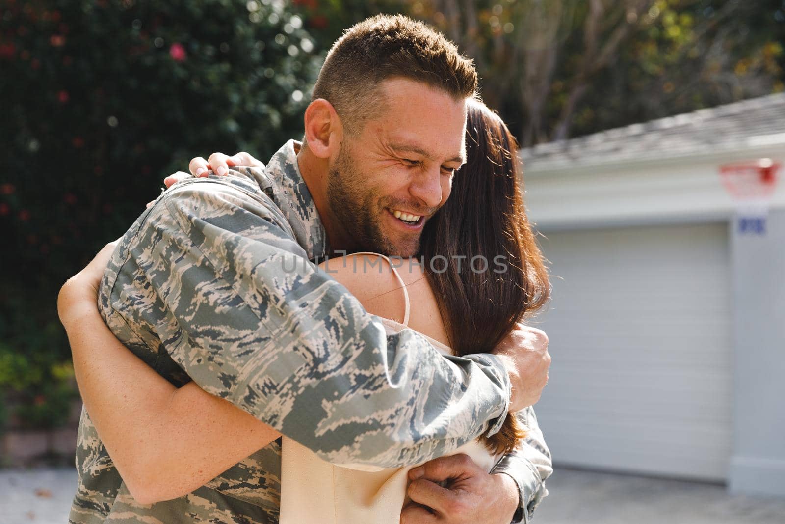 Caucasian male soldier hugging wife outside house decorated with american flag by Wavebreakmedia