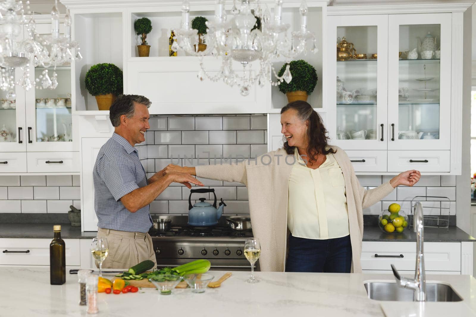 Happy senior caucasian couple in modern kitchen, dancing together and smiling. retirement lifestyle, spending time at home.