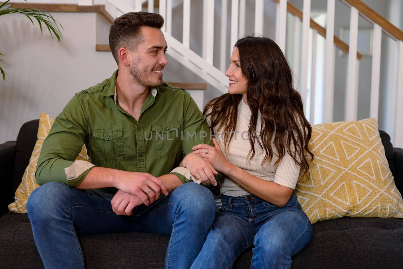 Happy caucasian couple sitting on sofa and looking at each other. lifestyle, leisure and spending free time at home.