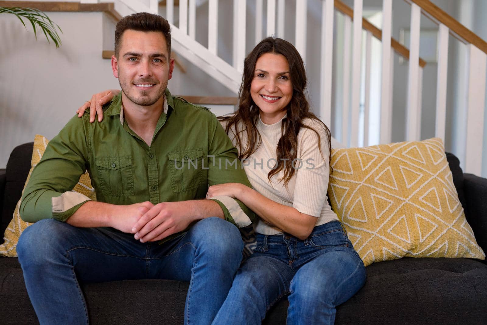 Happy caucasian couple sitting on sofa and looking at camera. lifestyle, leisure and spending free time at home.
