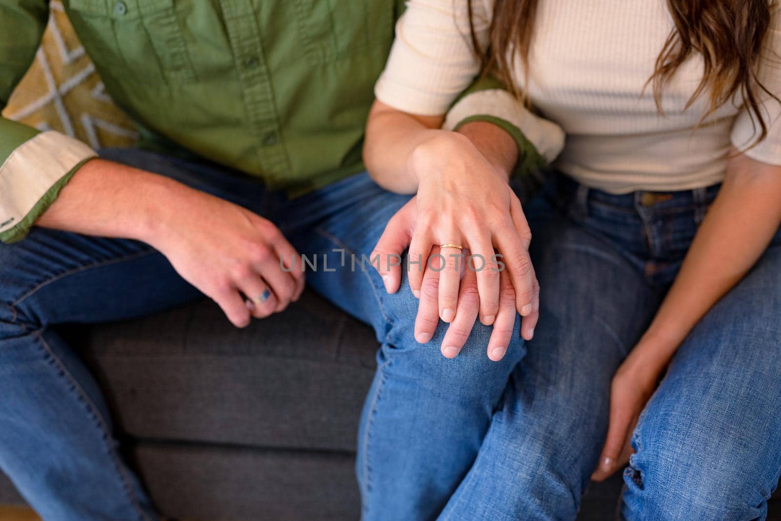 Hands of caucasian couple sitting on sofa and holding hands. lifestyle, leisure and spending free time at home.