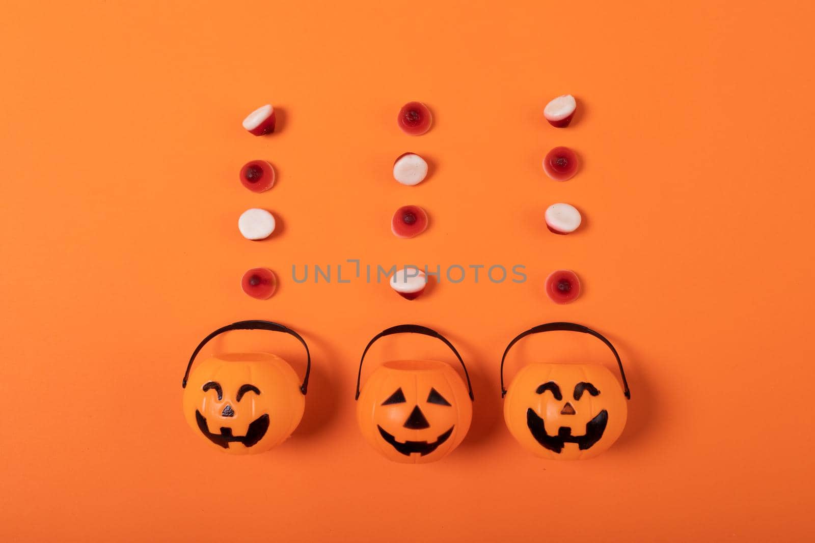 Halloween candies and three pumpkin shaped buckets against orange background. halloween festivity and celebration concept