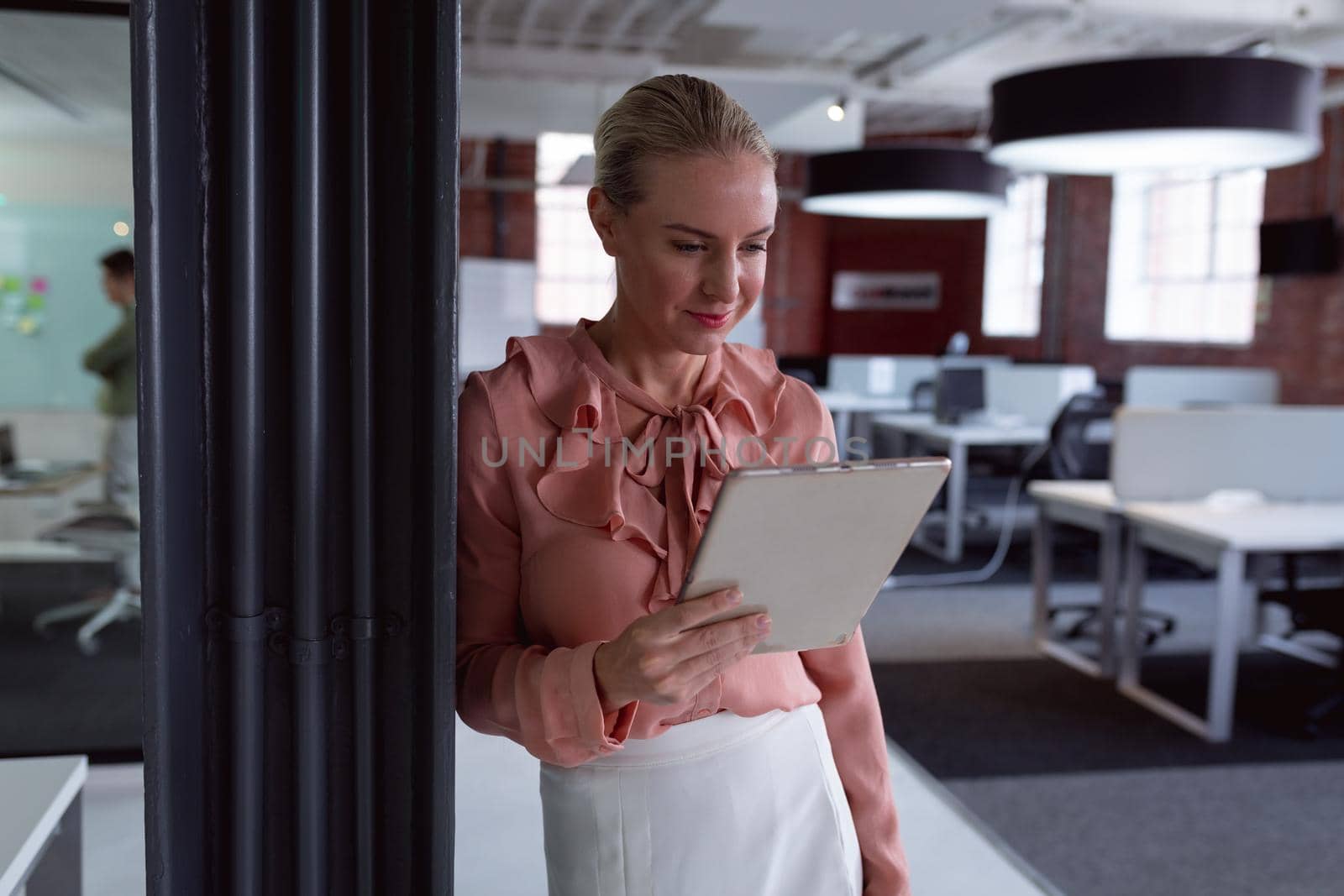 Happy caucasian businesswoman standing in office using tablet and smiling by Wavebreakmedia