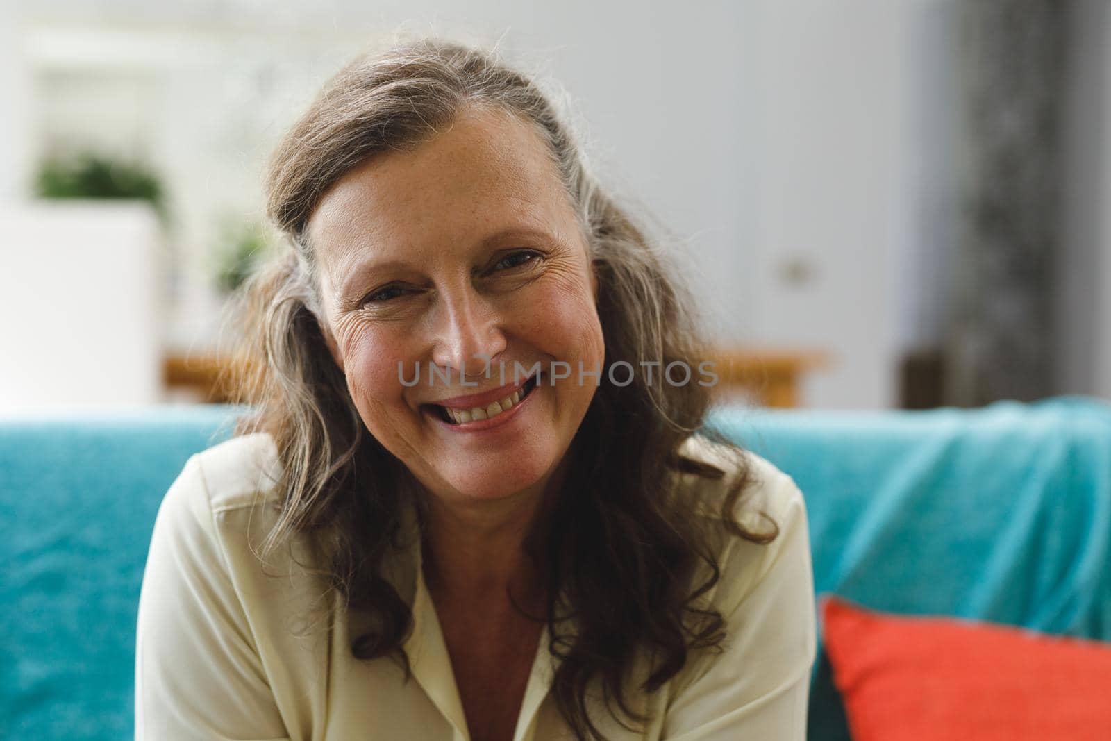 Portrait of happy senior caucasian woman in living room sitting on sofa, looking to camera. retirement lifestyle, spending time at home.