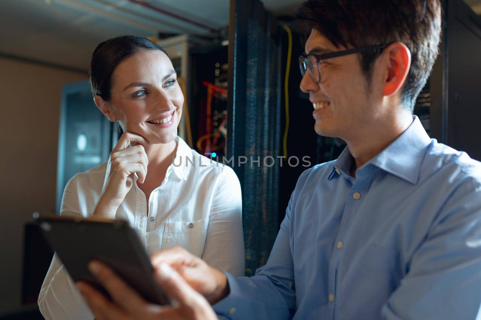 Diverse male and female engineers smiling while using digital tablet in computer server room by Wavebreakmedia