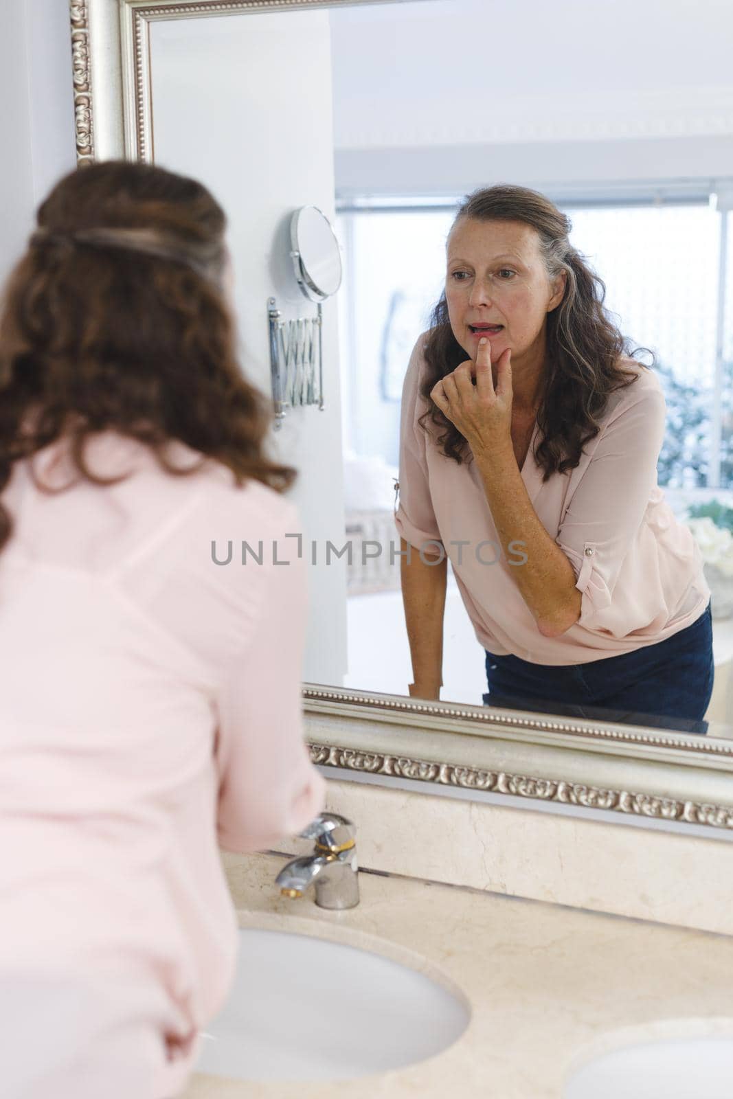 Senior caucasian woman in bathroom, looking at herself in mirror. senior caucasian woman in bathroom, looking at her face in mirror. retirement lifestyle and the aging process.