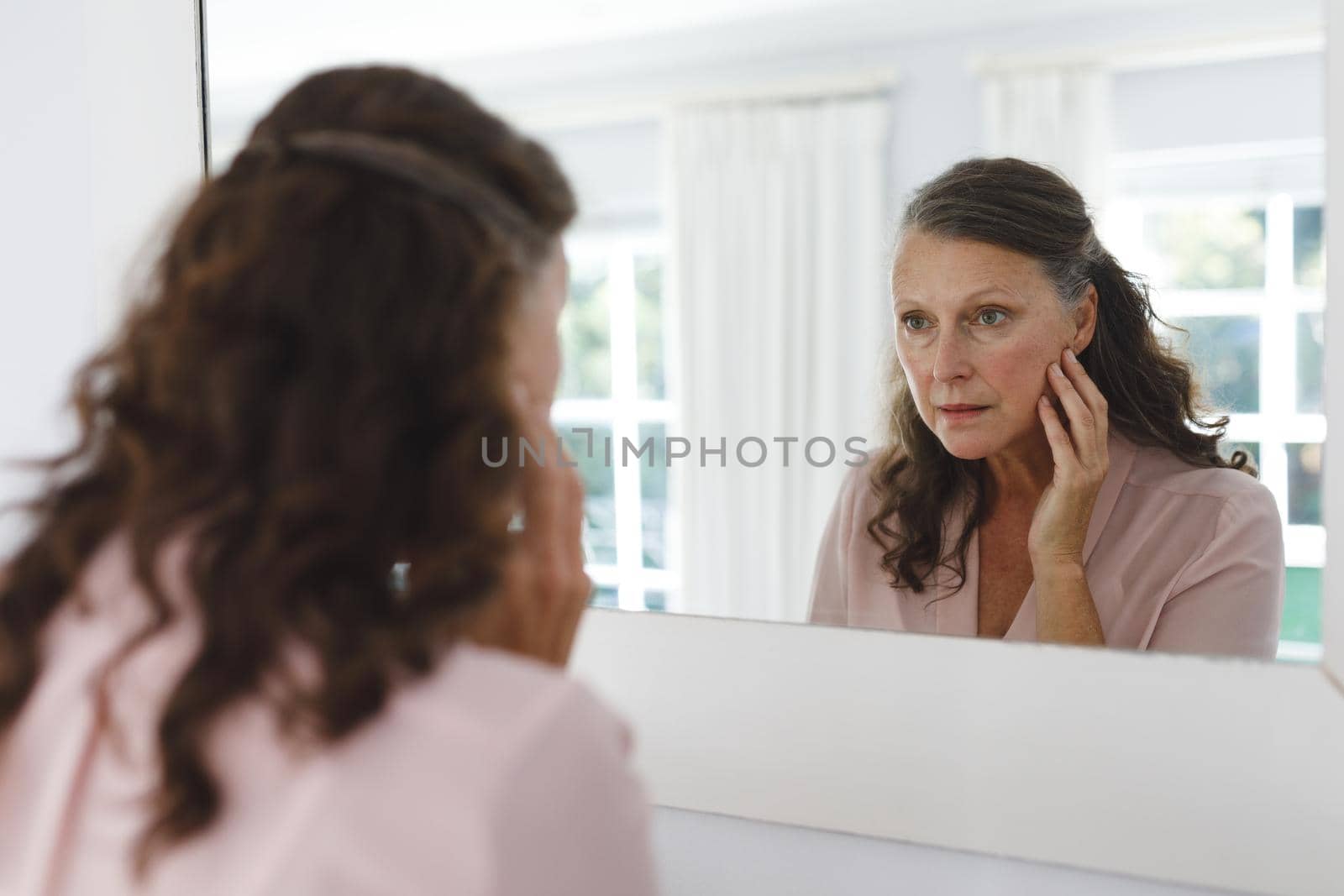 Senior caucasian woman in bathroom, looking at her face in mirror. retirement lifestyle and the aging process.