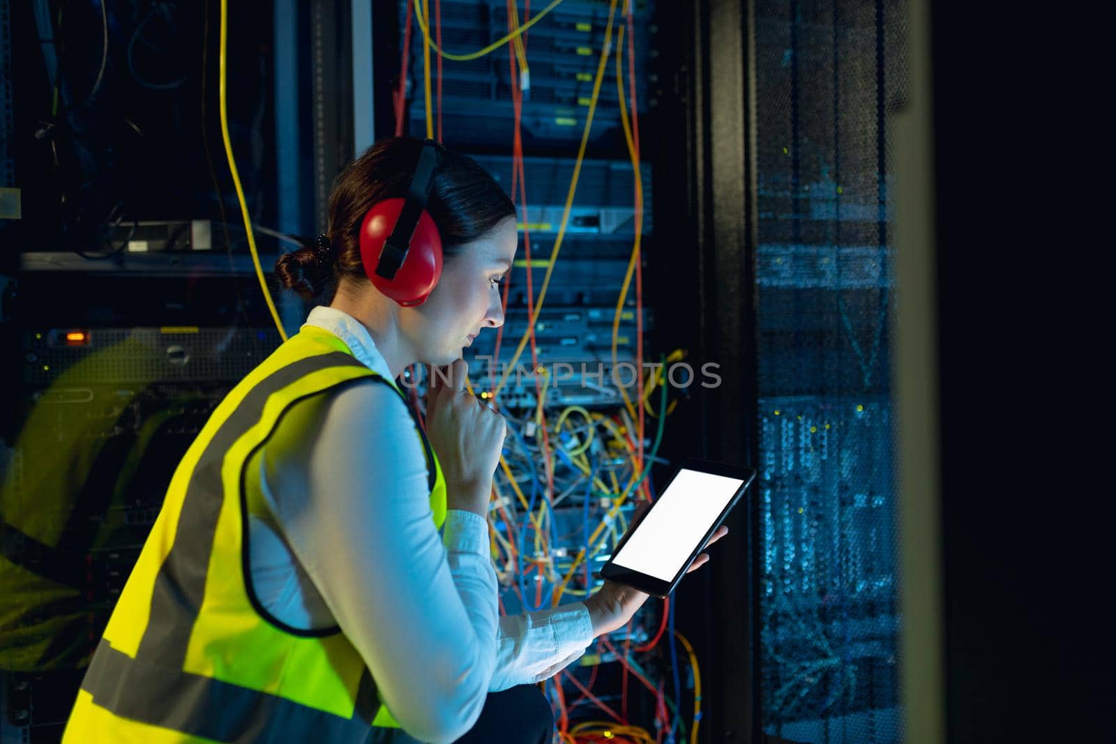 Thoughtful caucasian female engineer using digital tablet in computer server room. database server management and maintenance concept