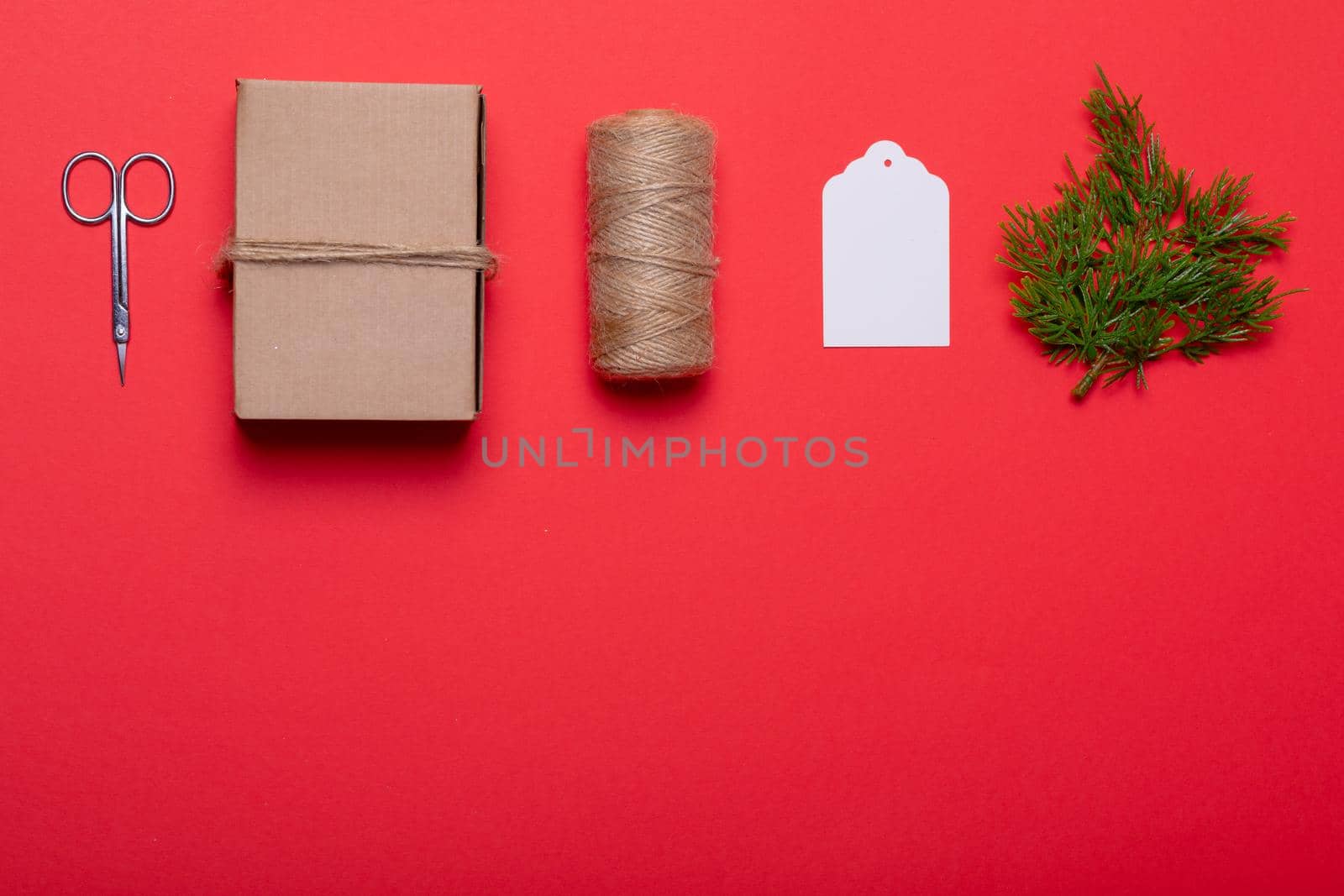 Composition of scissors, box, rope, card and tree branches on red background. christmas, tradition and celebration concept.