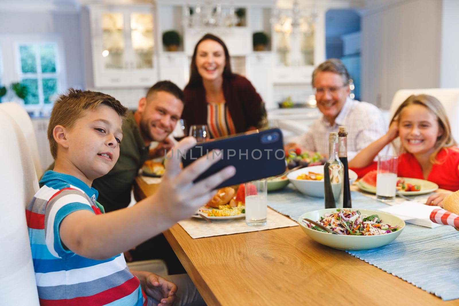 Caucasian grandfather and parents with daughter and son taking selfie while having dinner by Wavebreakmedia