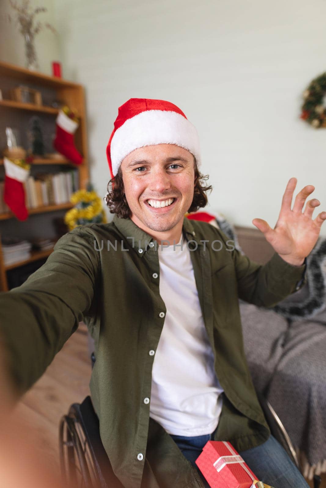 Portrait of caucasian disabled man in santa hat sitting on a wheelchair at home during christmas. christmas festivity and celebration concept