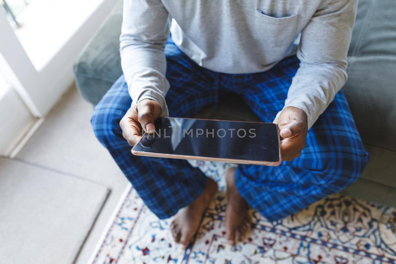 African american man using tablet and sitting on couch in living room. spending time alone at home with technology.