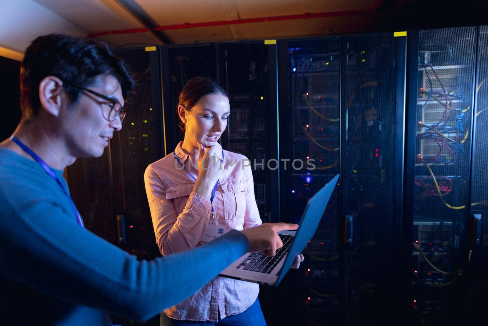 Diverse male and female engineers using laptop in computer server room. database server management and maintenance concept