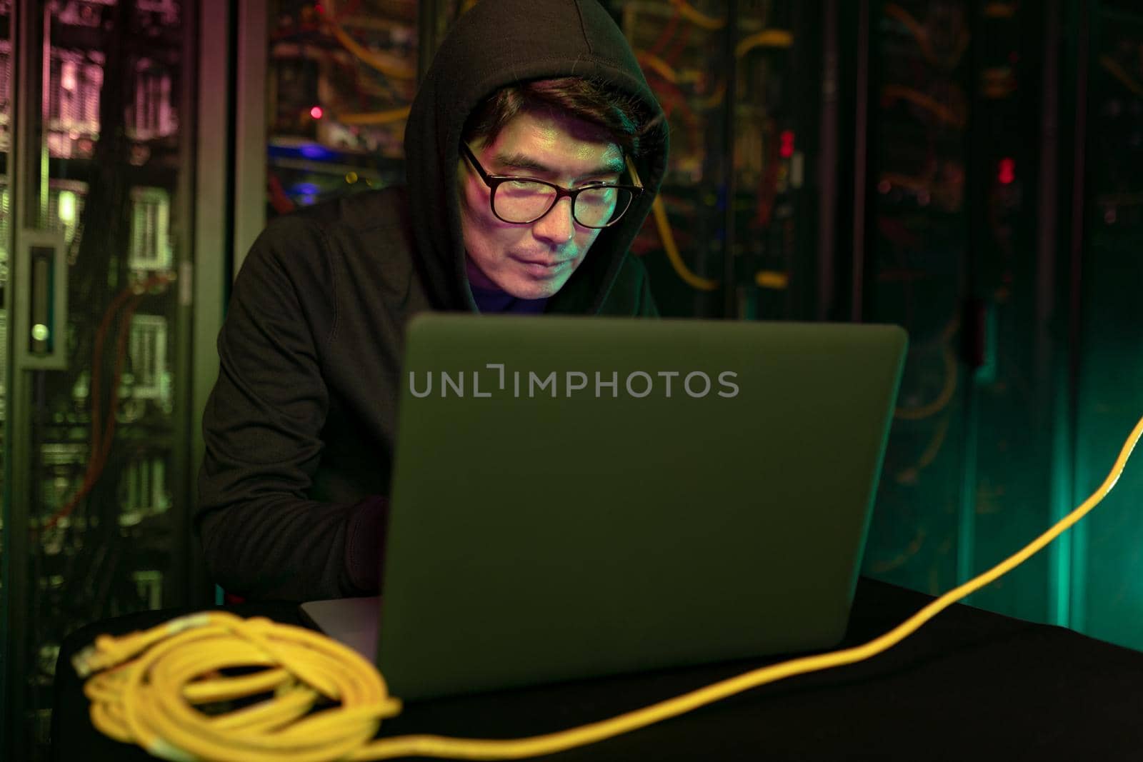 Asian male hacker using a laptop in computer server room by Wavebreakmedia