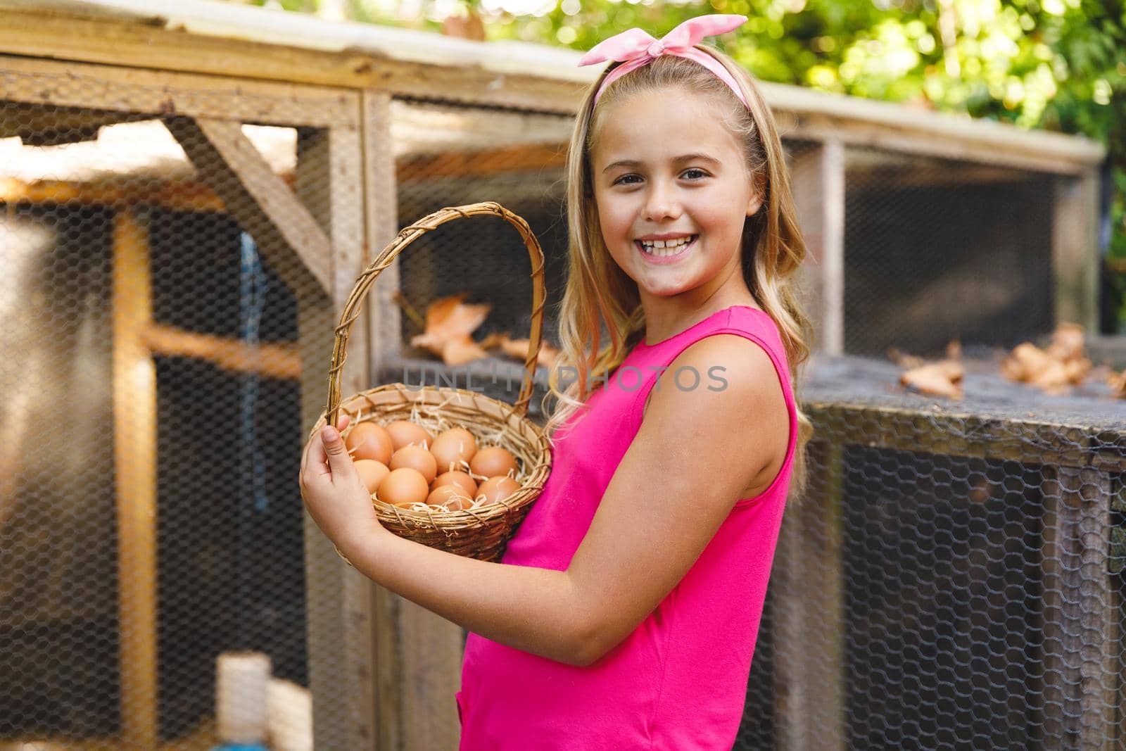 Portrait of smiling caucasian girl collecting eggs from hen house in garden. self sufficiency and spending time at home.