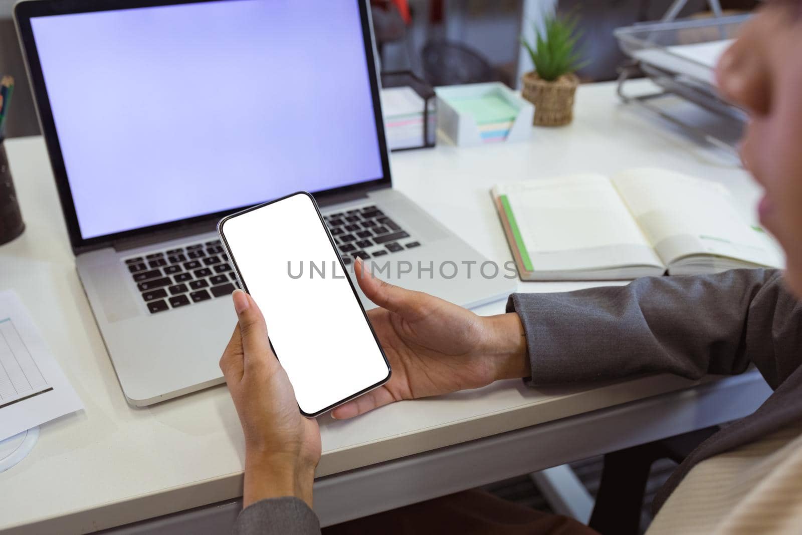 Biracial businesswoman sitting at desk using laptop and smartphone with copy space in modern office. business and office workplace.