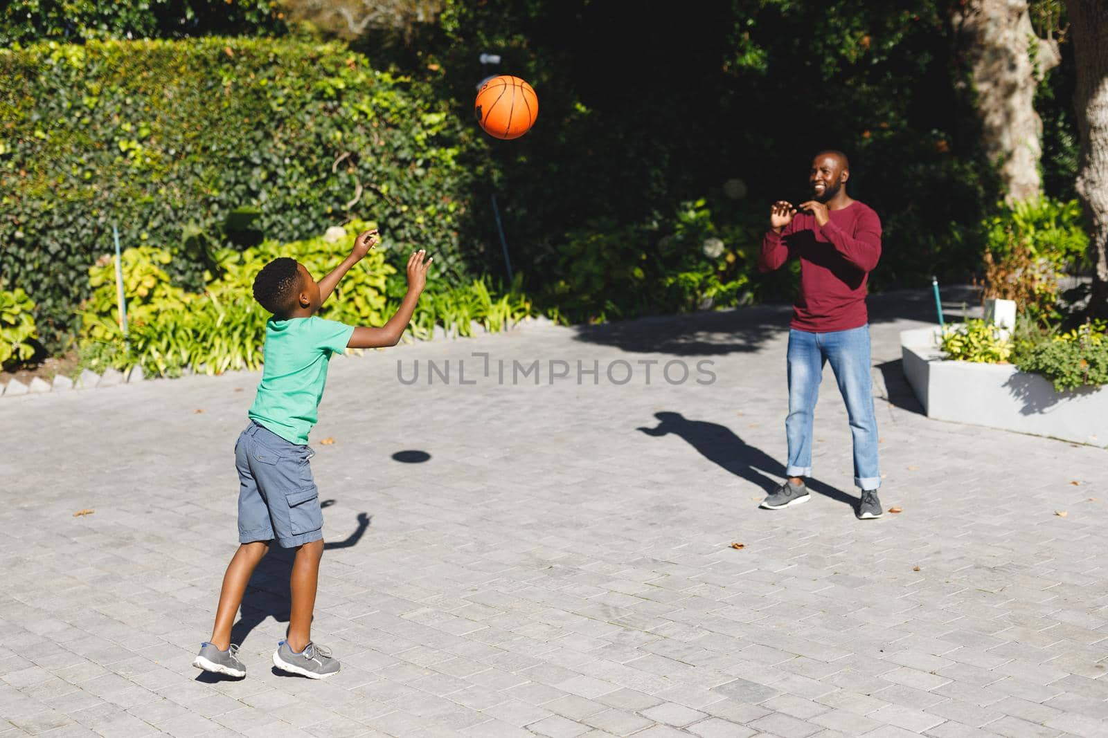 African american father with son smiling and playing basketball in garden. family spending time at home.