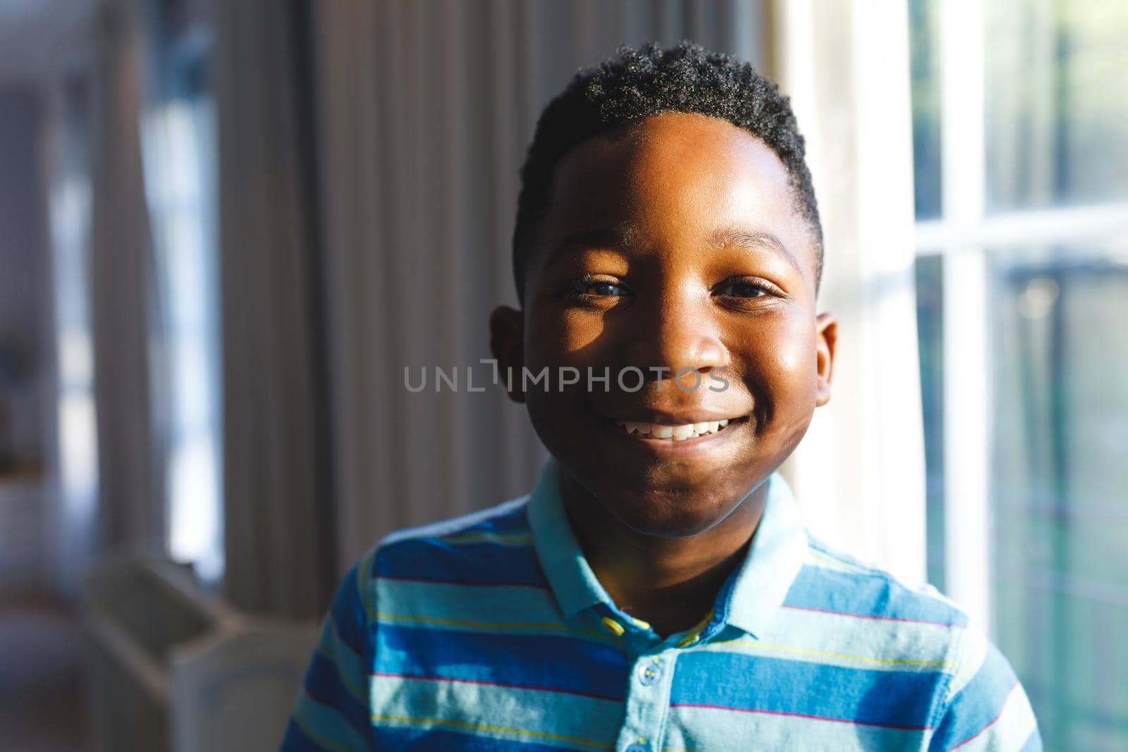 Portrait of african american boy looking at camera and smiling in living room. spending time alone at home.