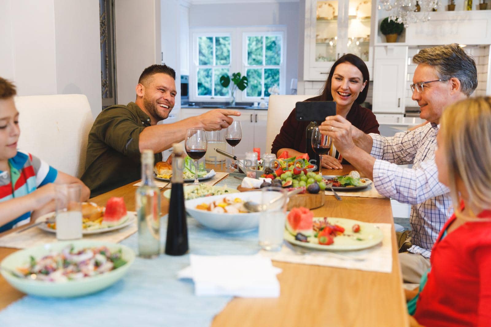 Smiling caucasian grandfather and parents with son and daughter sitting at table and having dinner. family spending time together at home.