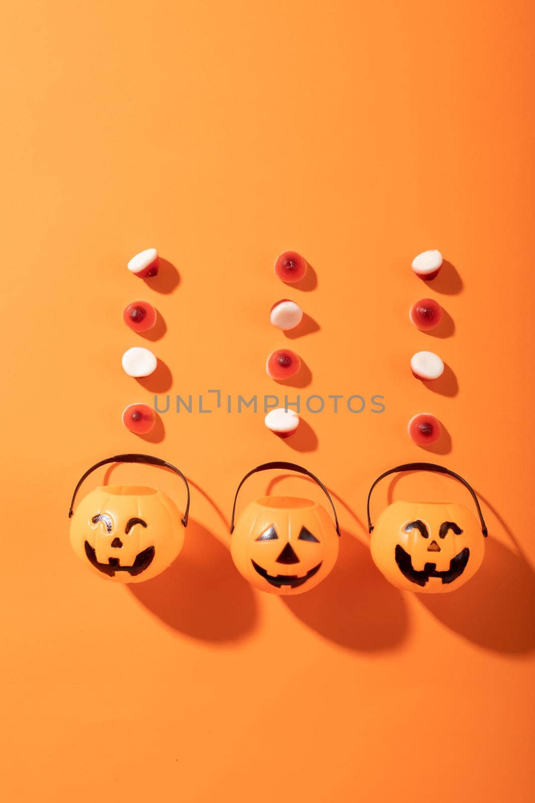 Halloween candies and three pumpkin shaped buckets against orange background by Wavebreakmedia