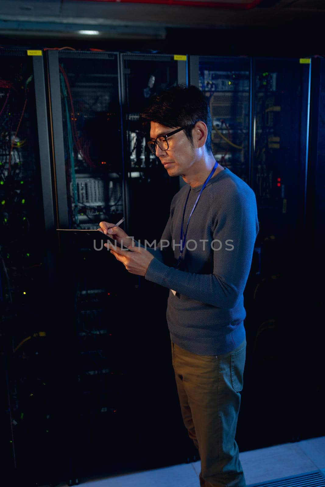 Asian male engineer writing on clipboard in computer server room. database server management and maintenance concept