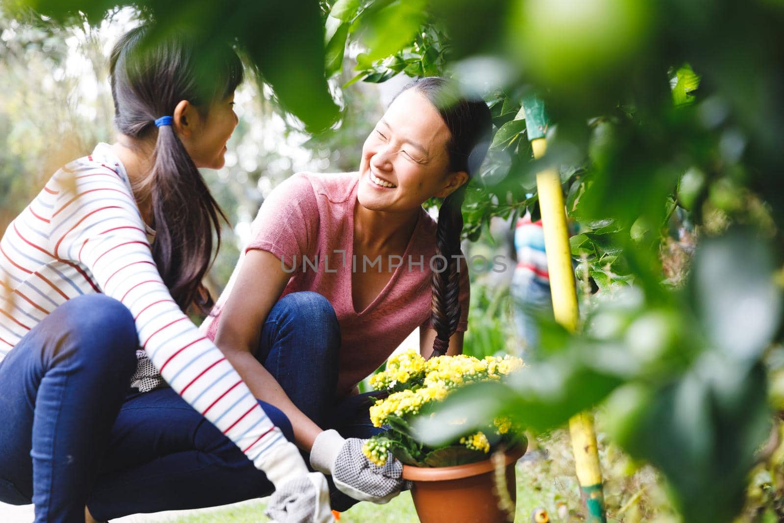 Happy asian mother and daughter smiling, wearing gloves and working in garden by Wavebreakmedia