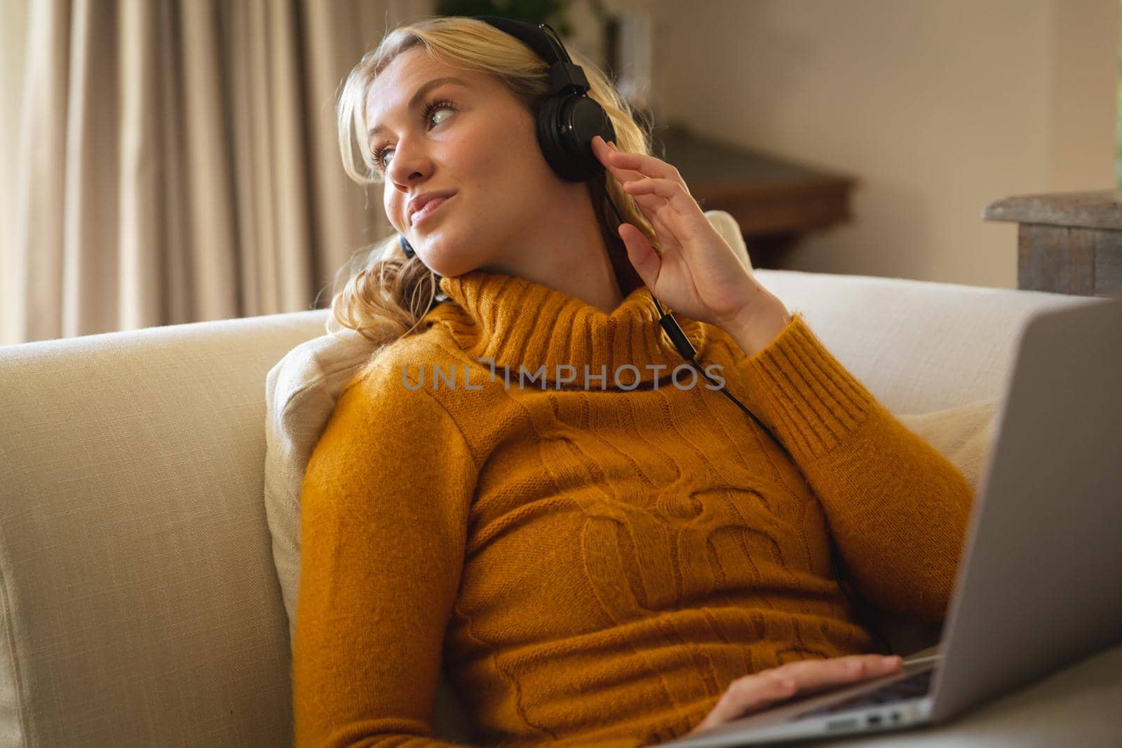 Smiling caucasian woman relaxing on couch in living room wearing headphones and using laptop. spending free time at home with technology.