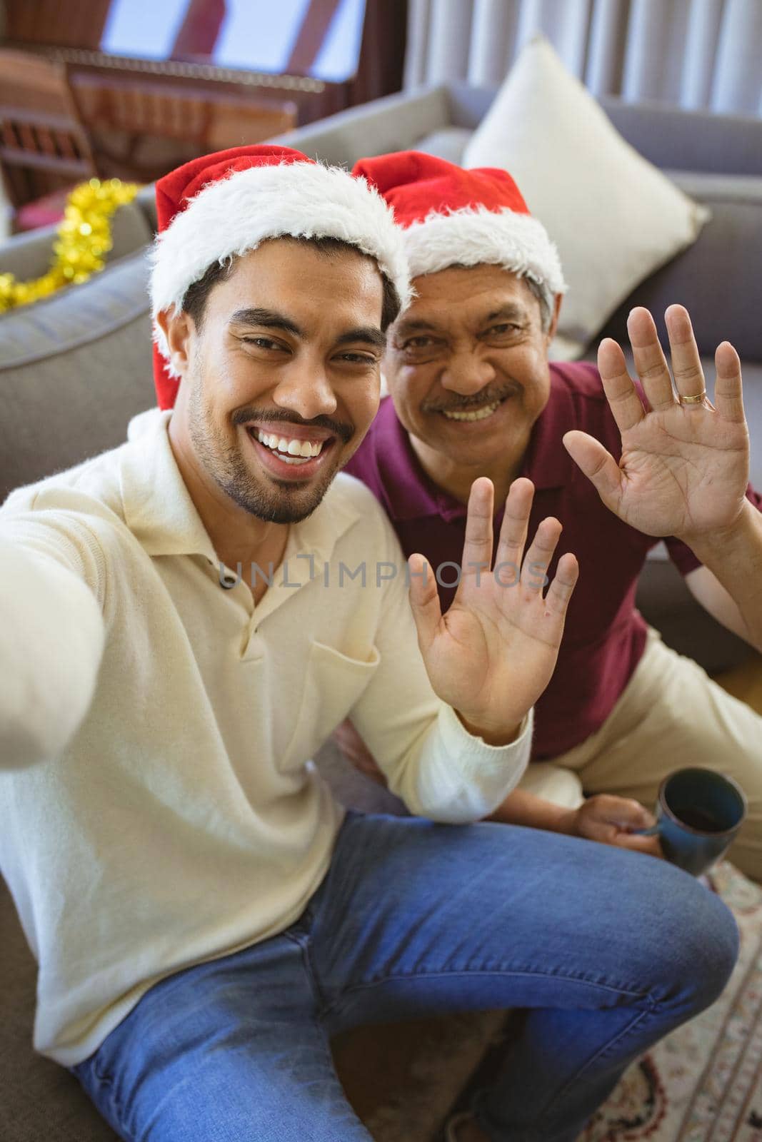 Portrait of happy biracial adult son and senior father in santa hats making christmas video call by Wavebreakmedia