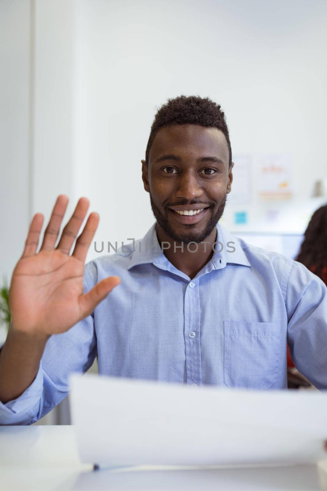 Smiling african american businessman sitting at desk making video call waving in modern office. business and office workplace.