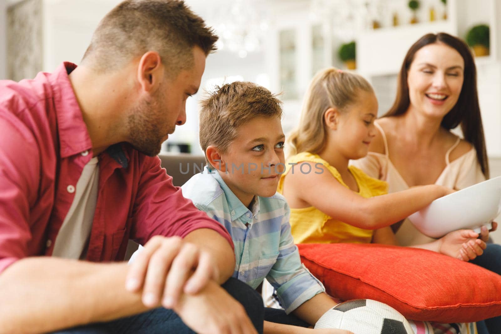 Happy caucasian parents, daughter and son sitting on couch talking and watching football match in tv by Wavebreakmedia
