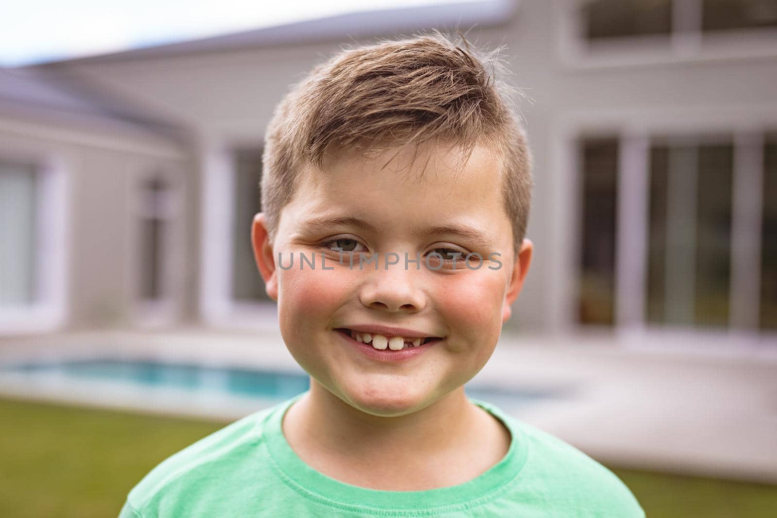 Portrait of smiling caucasian boy with brown hair standing at backyard outside house. childhood and home concept