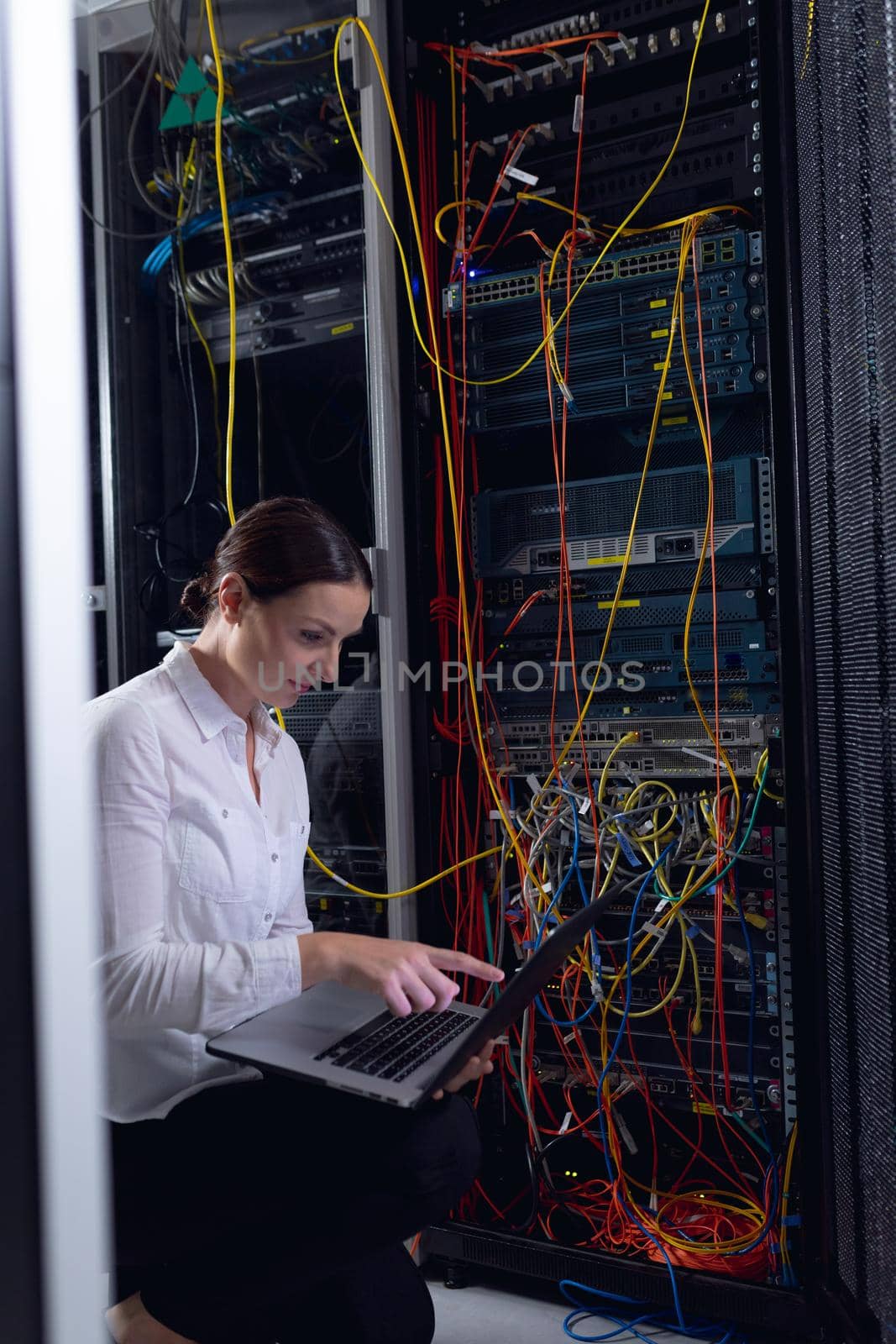 Caucasian female engineer with laptop inspecting computer server in computer server room. database server management and maintenance concept