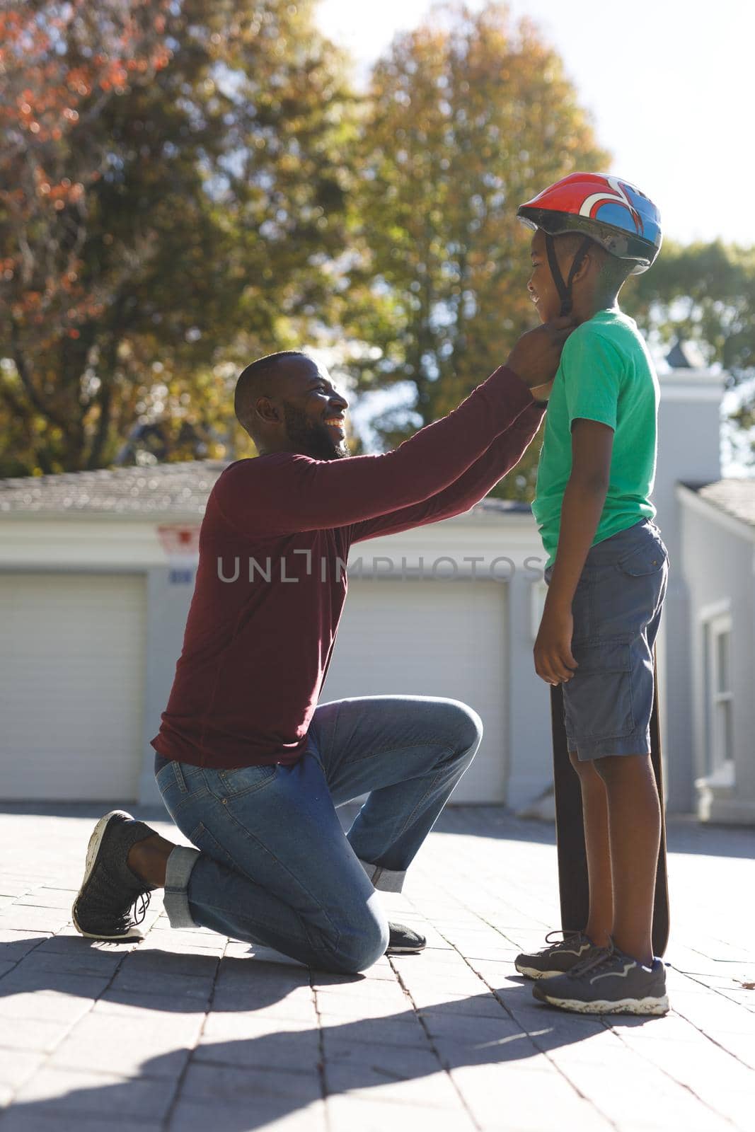 African american father with son smiling and preparing before skateboarding in garden. family spending time at home.
