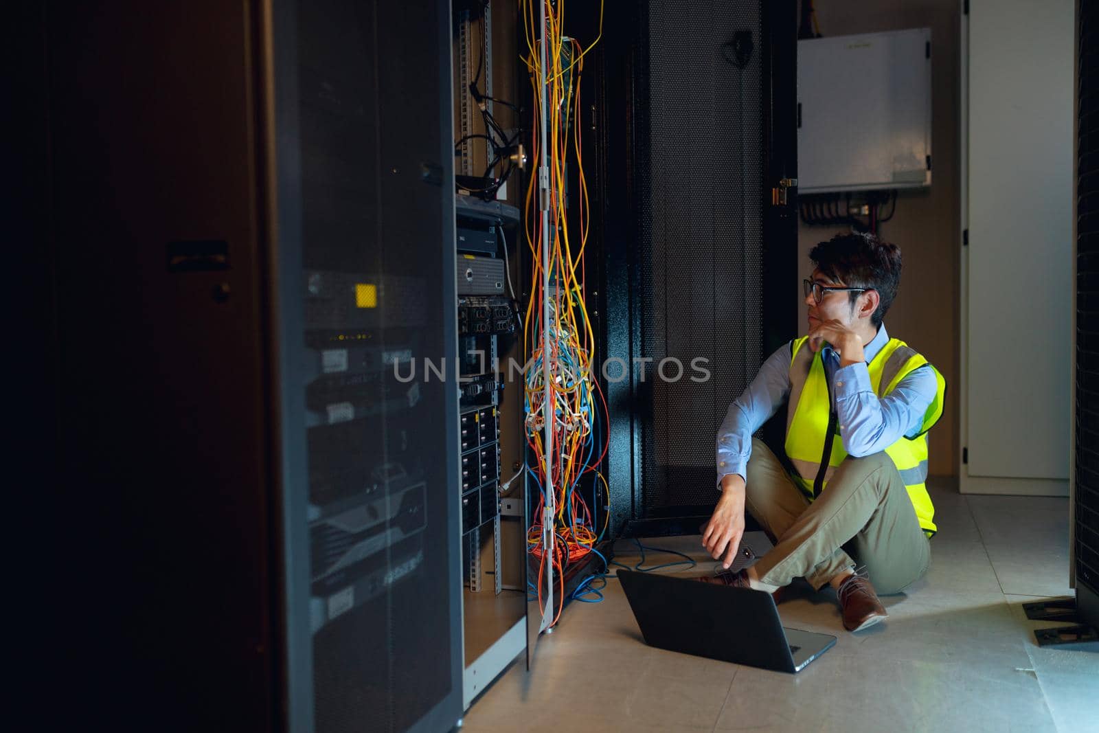 Asian male engineer wearing high visibility vest with laptop inspecting in computer server room by Wavebreakmedia