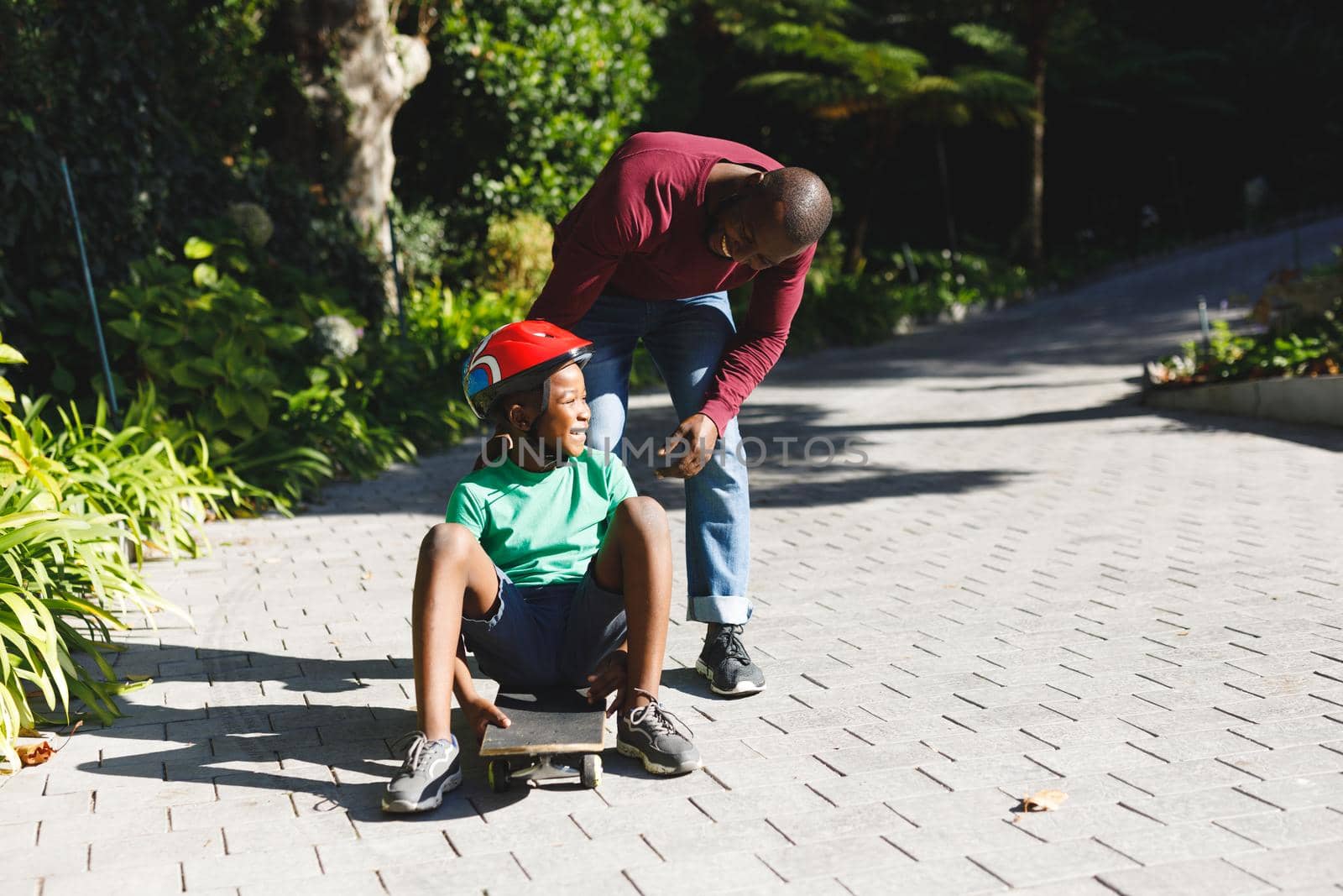 African american father with son smiling and playing with skateboard in garden by Wavebreakmedia