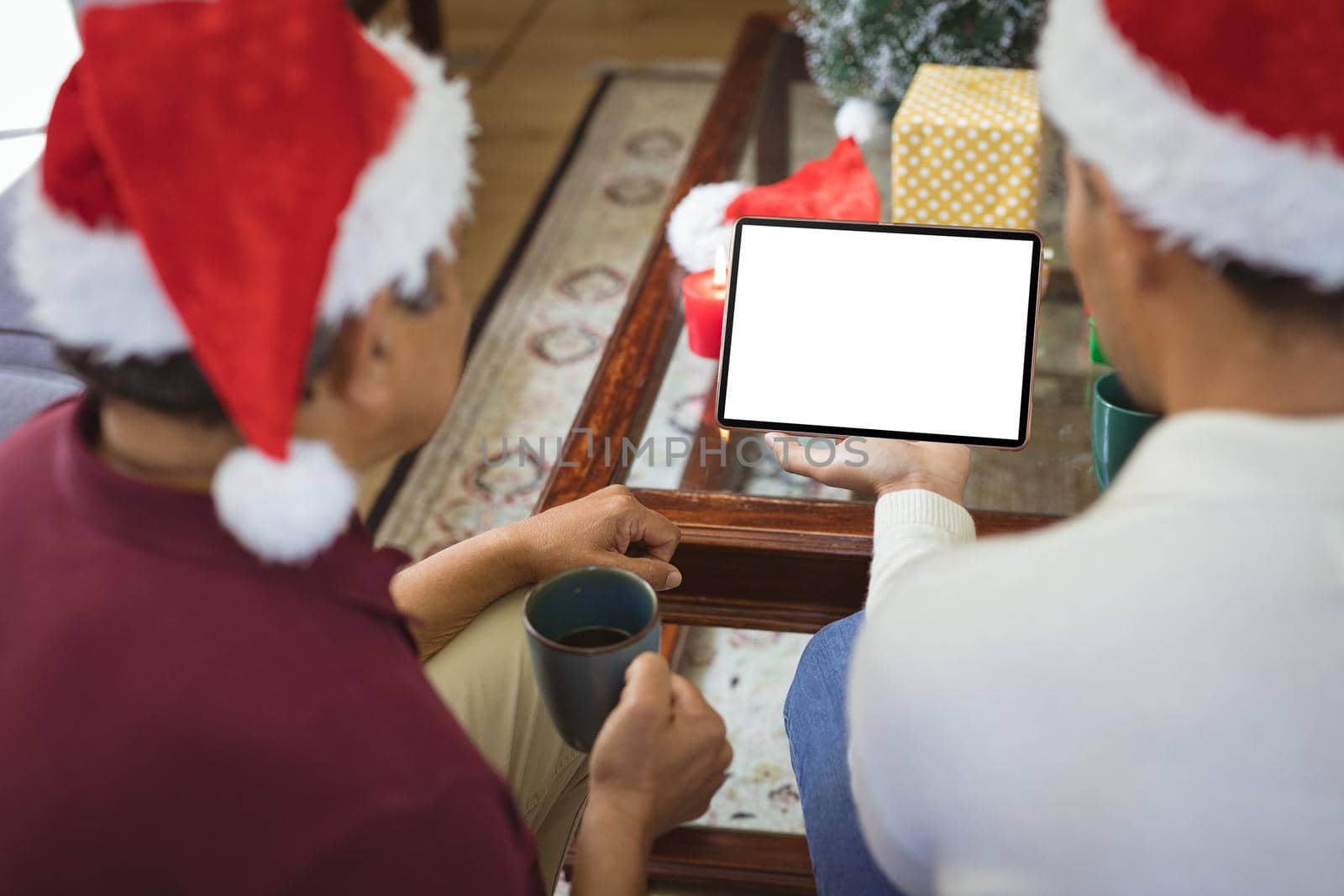 Biracial adult son and senior father in santa hats making tablet christmas video call. christmas, festivity and communication technology.
