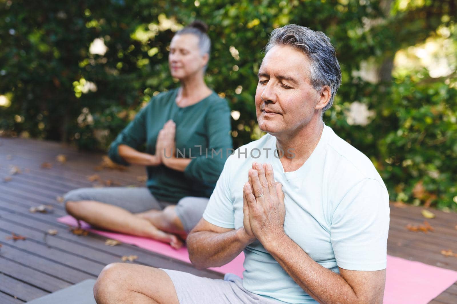 Happy senior caucasian couple practicing yoga, meditating in sunny garden. healthy retirement lifestyle, spending time at home.