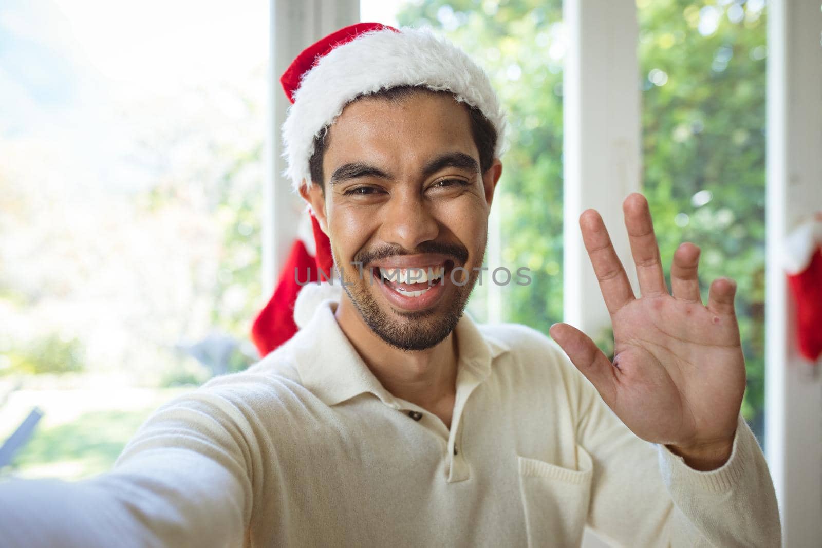Portrait of happy biracial man in santa hat making christmas video call. christmas, festivity and communication technology.