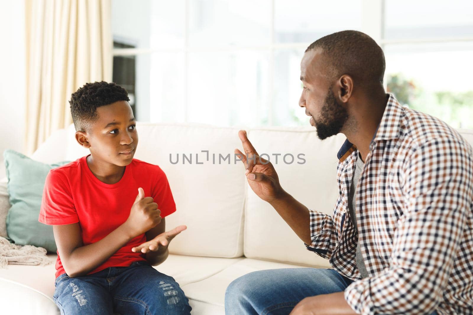Happy african american father with son sitting on couch in living room talking sign language. father and son communicating without words.