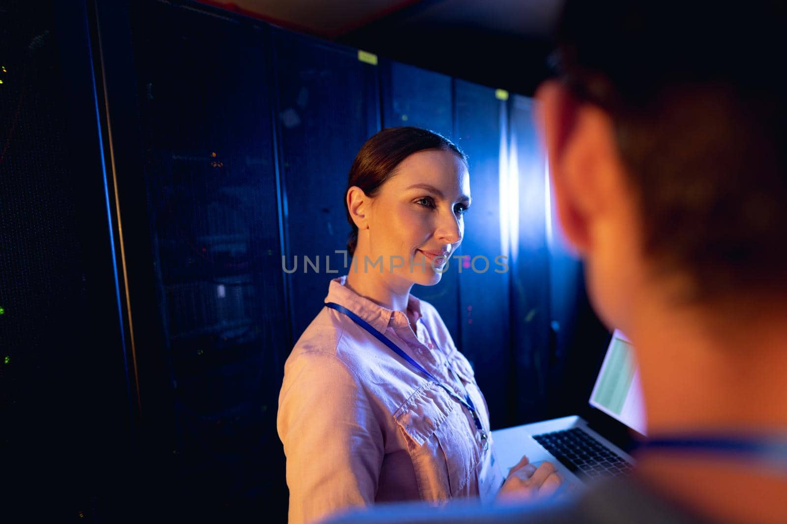 Caucasian female engineer using laptop in computer server room. database server management and maintenance concept