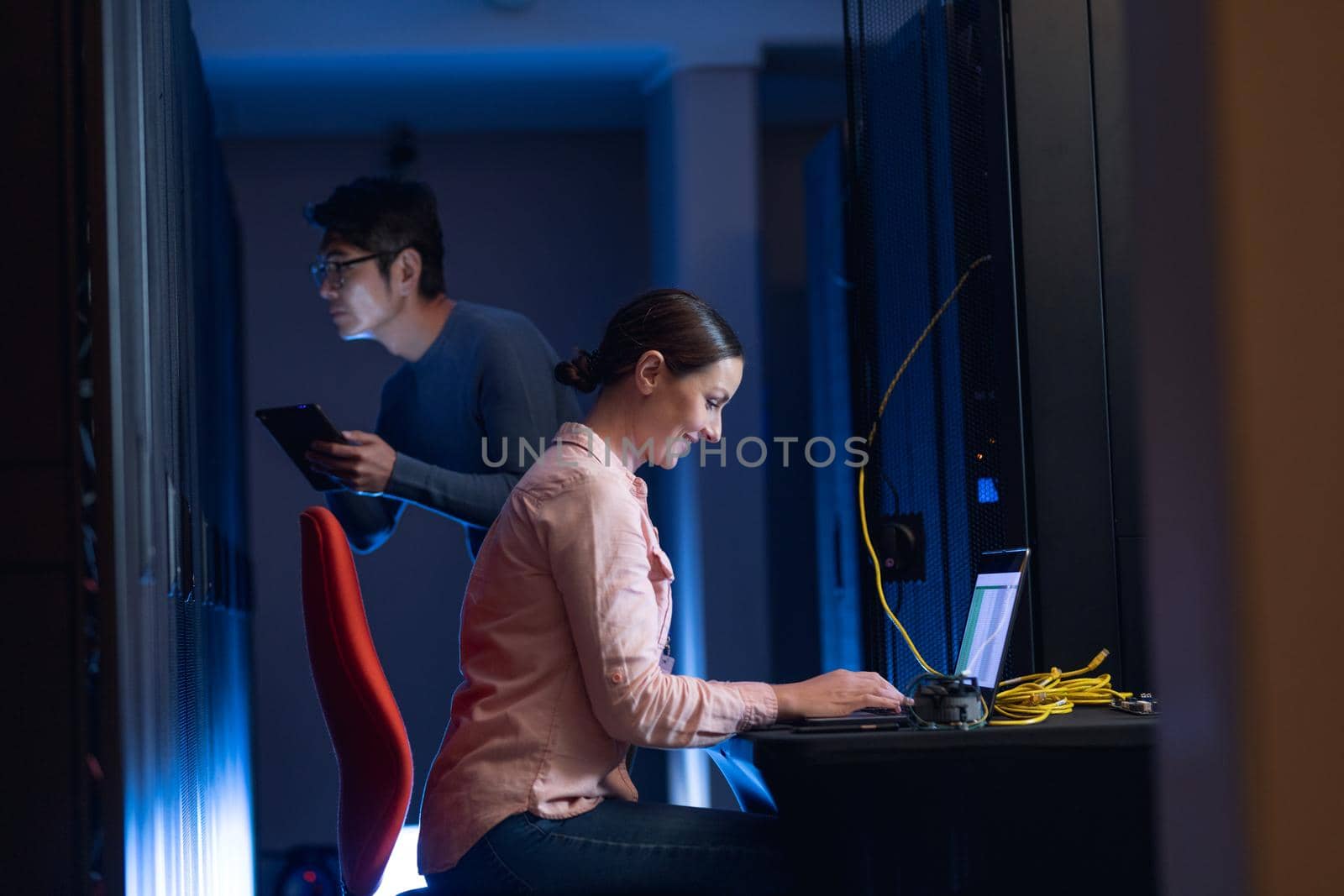 Caucasian female engineer using laptop and asian male engineer inspecting in computer server room. database server management and maintenance concept
