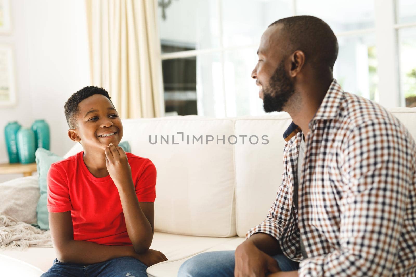 Happy african american father with son sitting on couch in living room talking sign language. father and son communicating without words.