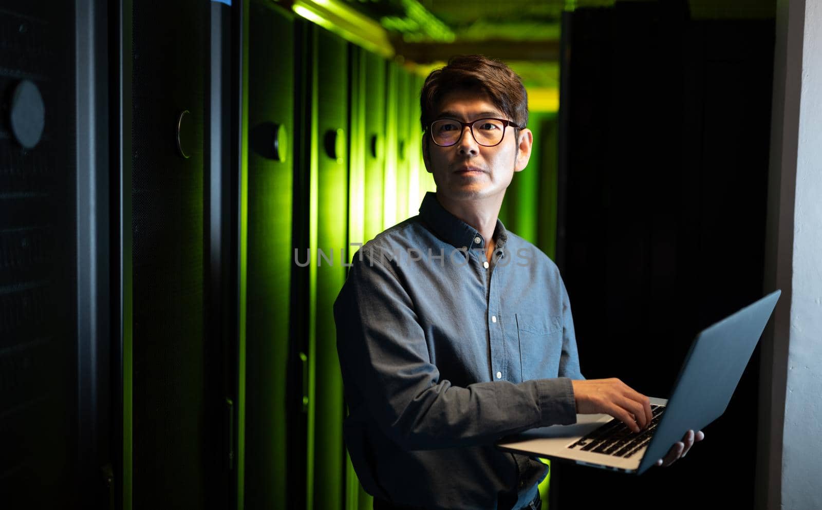 Asian male engineer using laptop in computer server room. database server management and maintenance concept