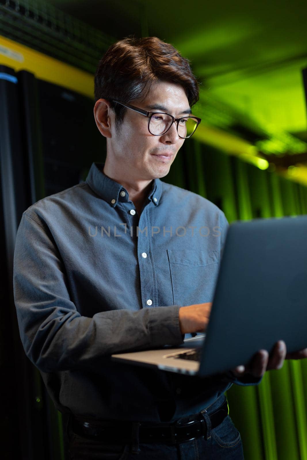 Asian male engineer using laptop in computer server room by Wavebreakmedia