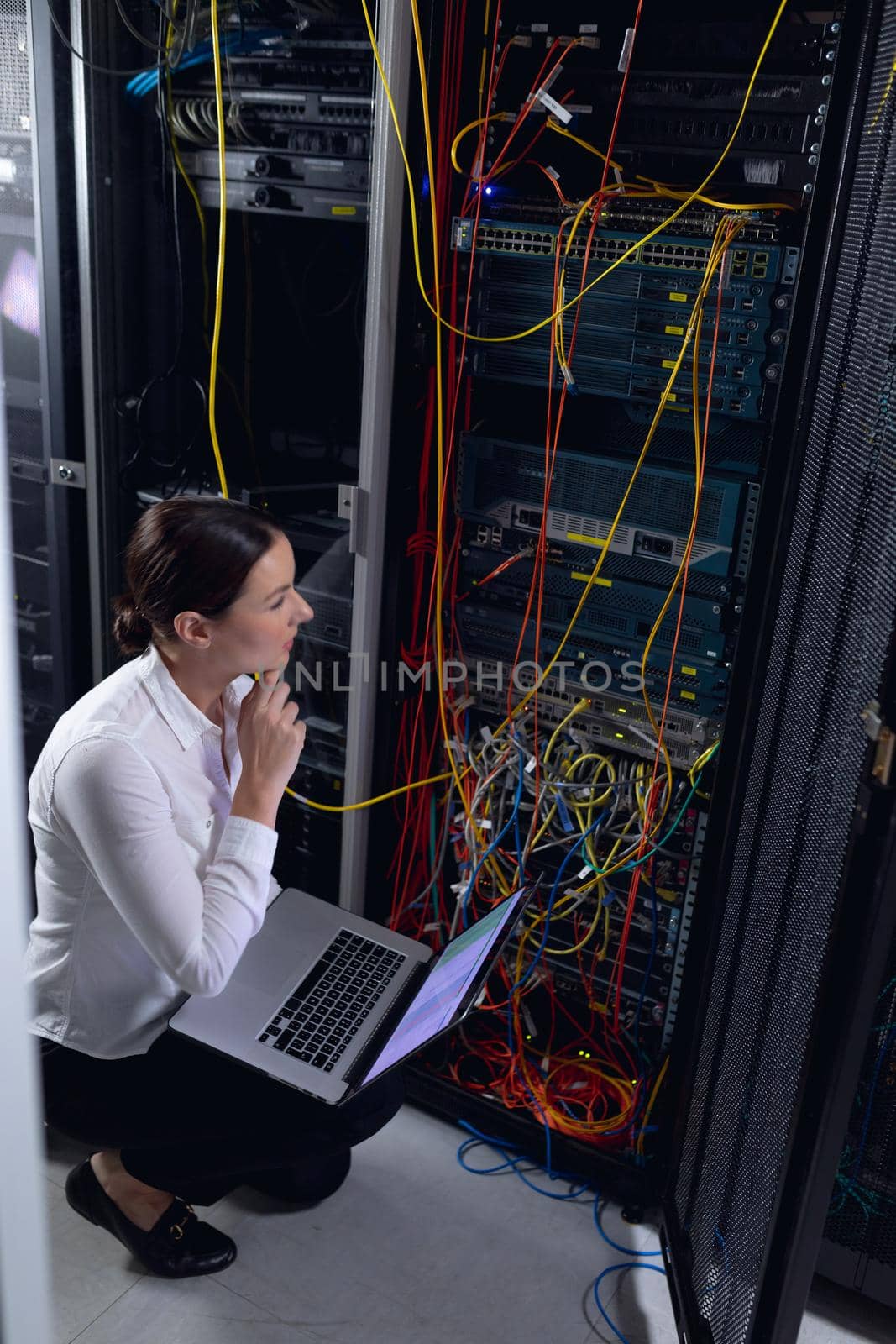 Thoughtful caucasian female engineer with laptop inspecting computer server in computer server room. database server management and maintenance concept