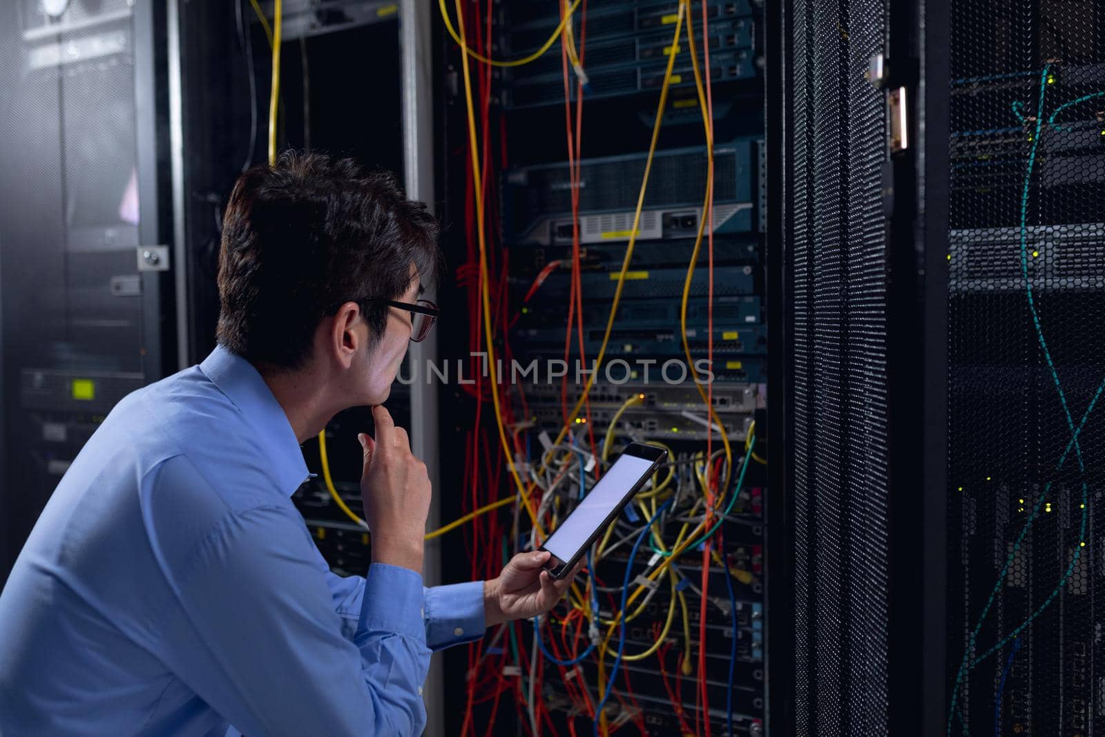 Thoughtful asian male engineer using digital tablet and inspecting computer server in server room by Wavebreakmedia