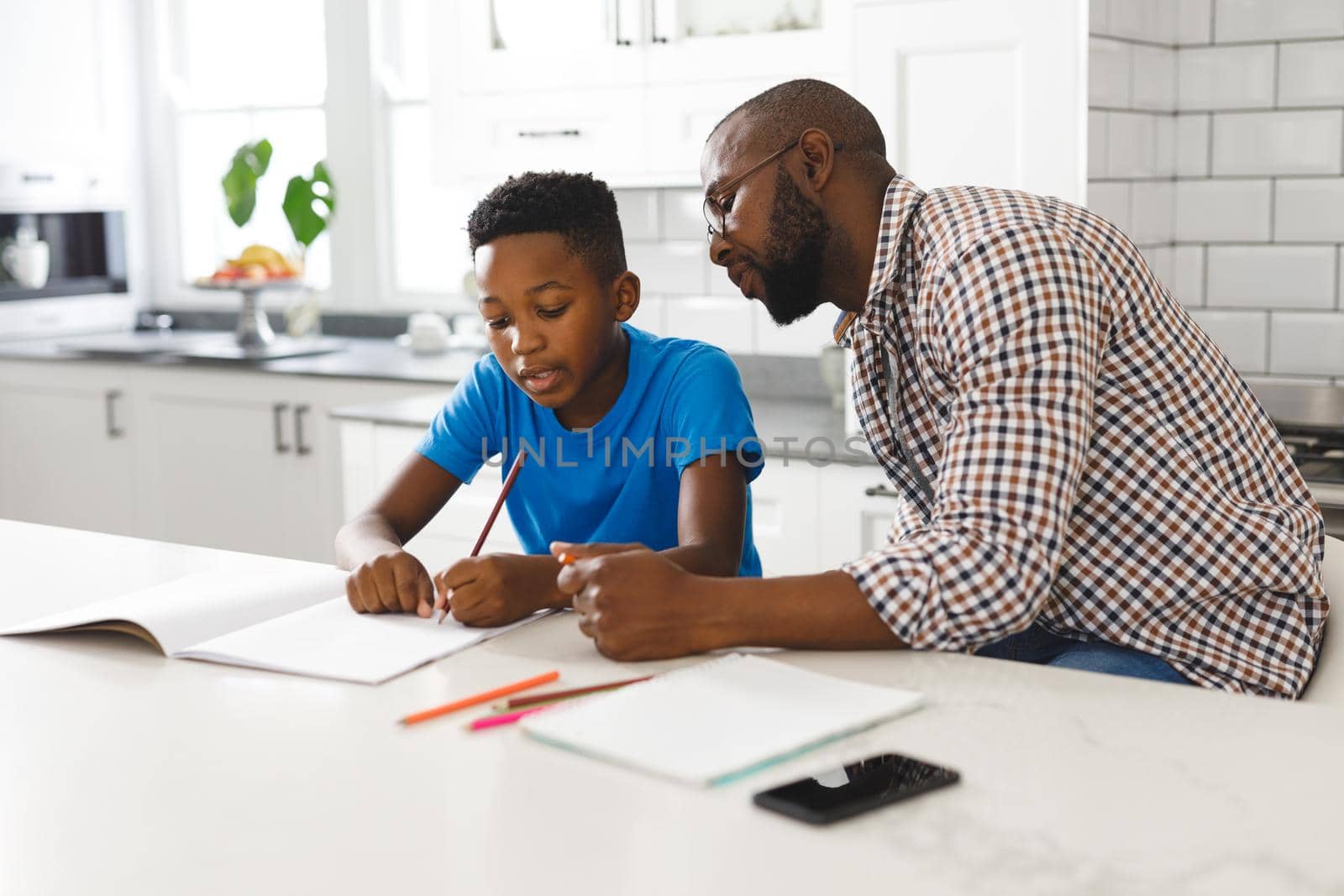 African american father and son in kitchen, doing homework together by Wavebreakmedia