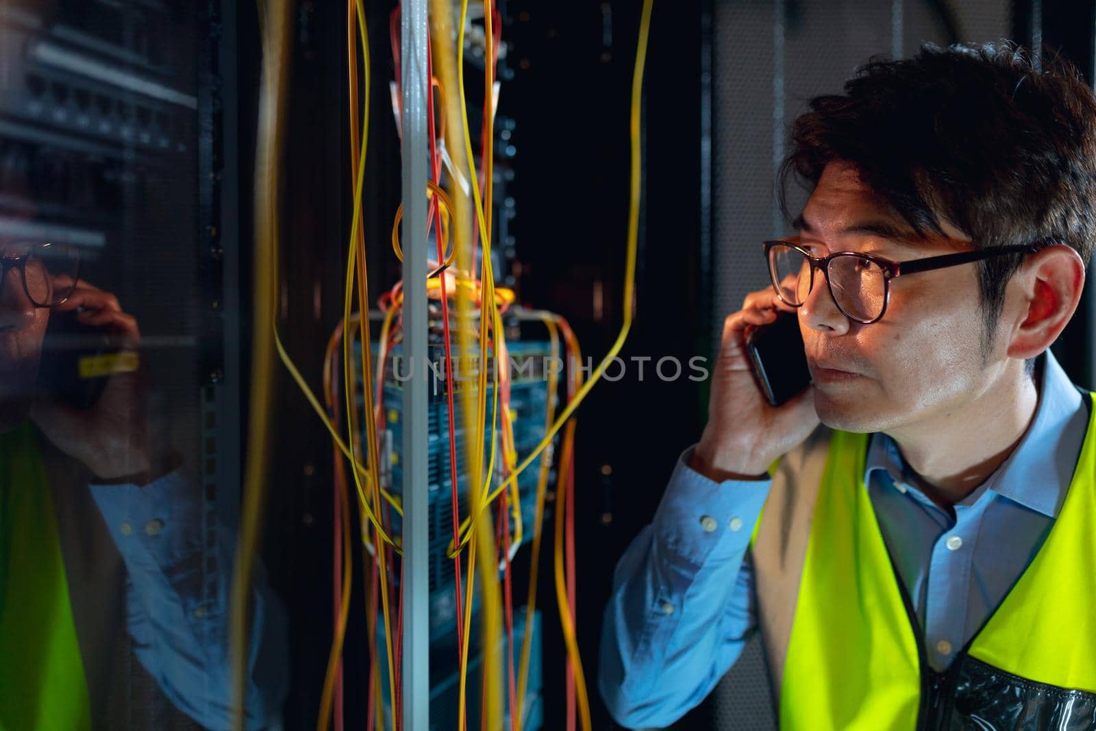 Asian male engineer talking on smartphone while inspecting in computer server room. database server management and maintenance concept